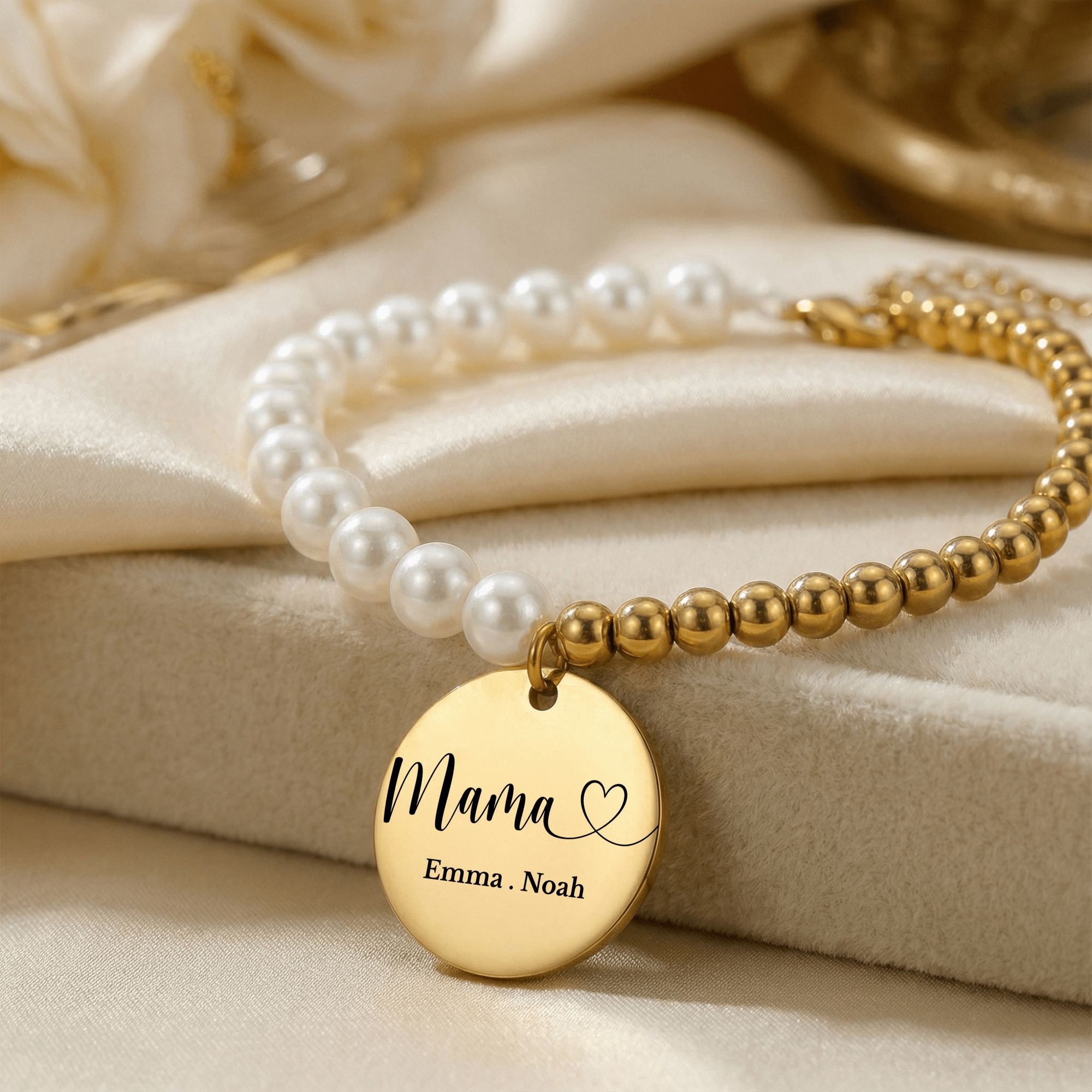 Goldenes Perlenarmband mit graviertem Mama-Anhänger auf weißem Satin – Detailansicht